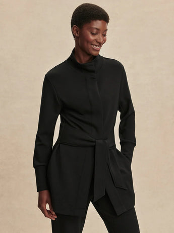 Front view of the black Varley Anset Jacket, showing the tied waist, high collar and side pockets.