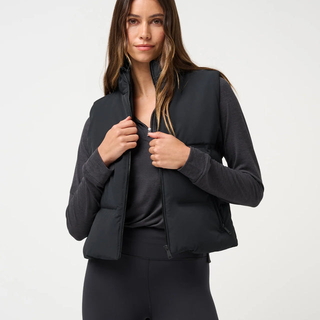 Front view of black TravisMathew Moontide Bonded Vest 2.0 worn open over a long-sleeve top.