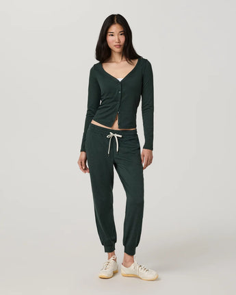Model wearing the Vuori Halo V-Neck Cardigan in Hemlock Heather with matching joggers and white sneakers.
