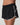 Close-up of Vuori Clementine Retro Shorts in Black, showing the elastic waistband, white piping and Vuori logo.
