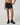Front view of Vuori Clementine Retro Shorts in Black, showing the gathered waistband and white-trimmed hems