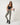 Model wearing TravisMathew Pulse Leggings in Olive Smoke with a black cropped tank and sneakers.