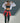 Model outdoors wearing the Vuori Daily Layered Bra in Ink with white contrast trim, an open white jacket and matching leggings.