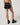 Back view of Vuori Clementine Retro Shorts in Black, showing white contrast piping and curved hems