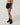 Angled side view of Vuori Clementine Retro Shorts in Black, showing the curved hem, white piping and small logo.