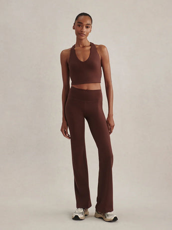 Model wearing Varley Always Flare leggings in Mahogany with a matching sports bra and sneakers.